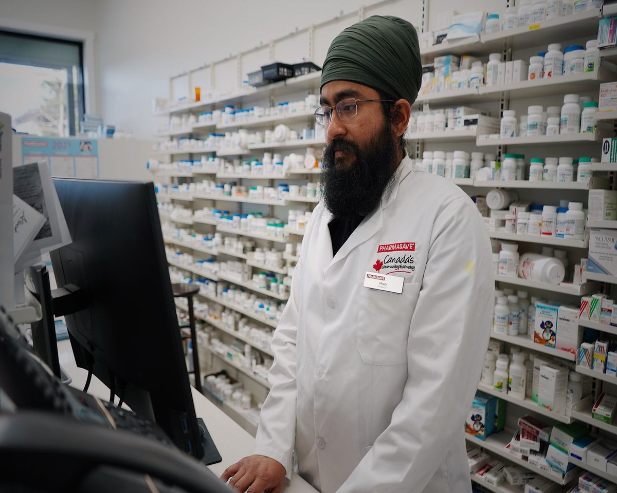 Pharmacist checking a delivery record on screen in front of stocked shelves